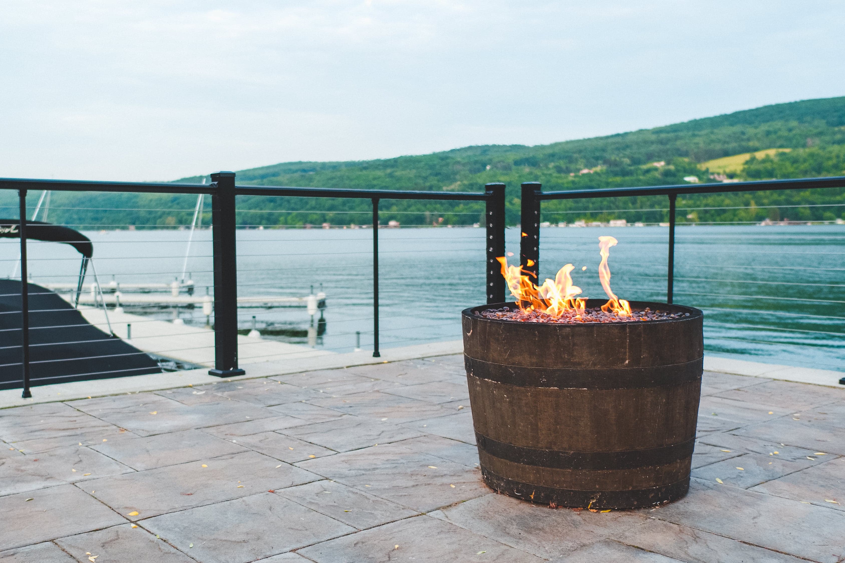 The gas fire pit burning in its whiskey barrel on the stone terrace at the water's edge, with the docks and Keuka Lake beyond