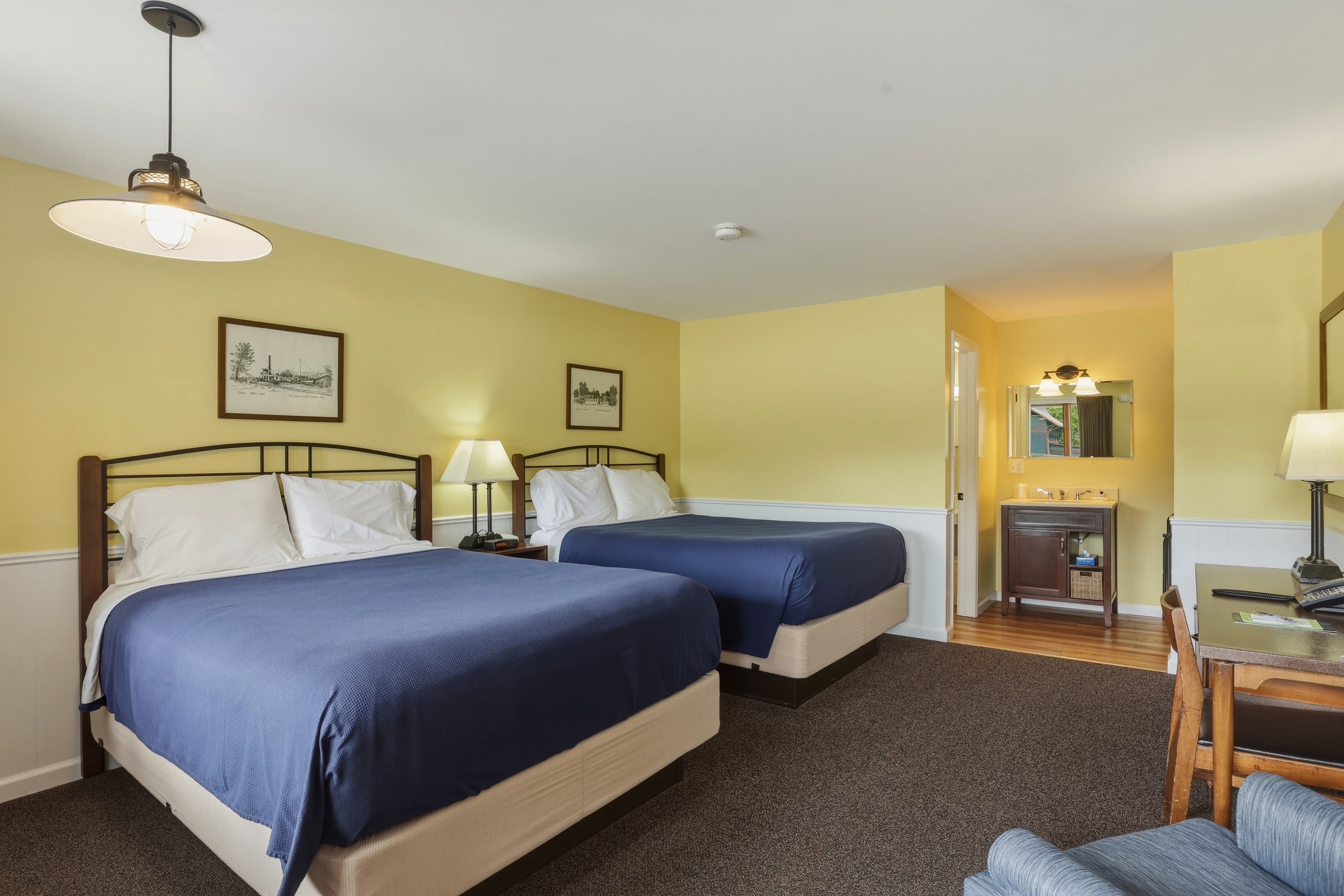 Double queen room — two queen beds under framed prints, with the vanity alcove beyond